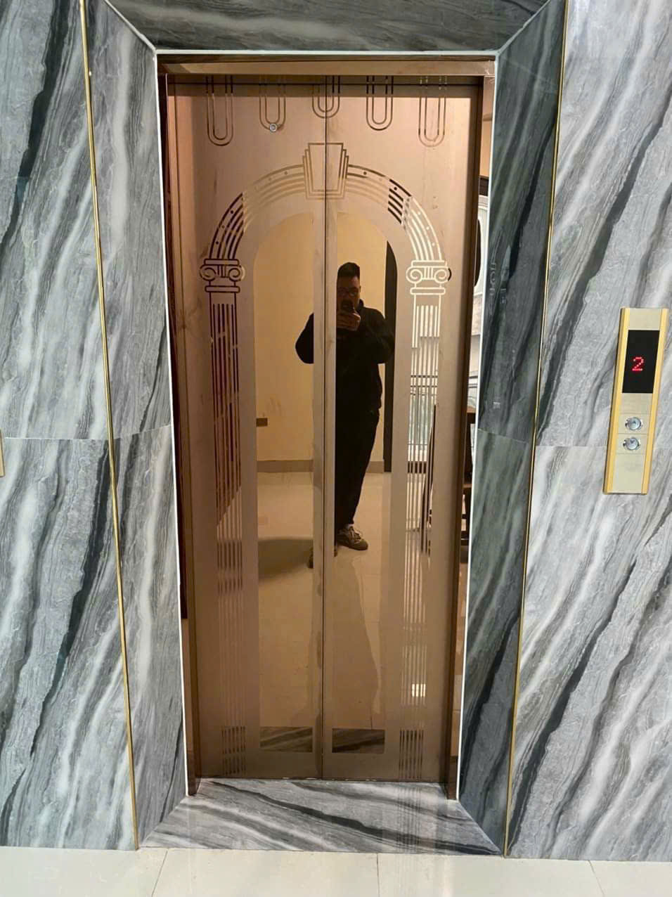 Thang máy cửa kính hoa văn cổ điển trong sảnh ốp đá marble sang trọng